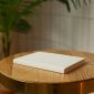 Closed book with clean white hardcover placed on round wooden table in light room with green potted plant on blurred background